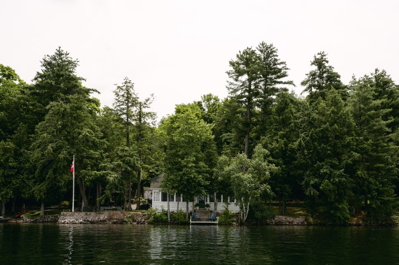 Home Serene waterfront cottage surrounded by lush forest on a clear summer day in Ontario, Canada.